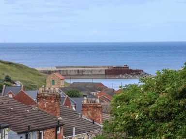 A coastal view with brick houses and chimneys in the foreground and a stone pier extending into the sea at Lady Bird Retreat in Skinningrove