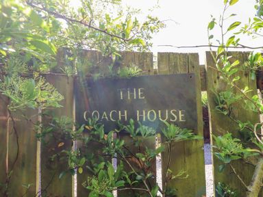 A wooden fence with a sign that says The Coach House surrounded by green plants at The Coach House in Lowick near Holy Island
