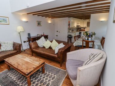 A living room with brown leather sofas a wooden coffee table a round upholstered chair and a dining table with chairs at The Coach House in Lowick near Holy Island