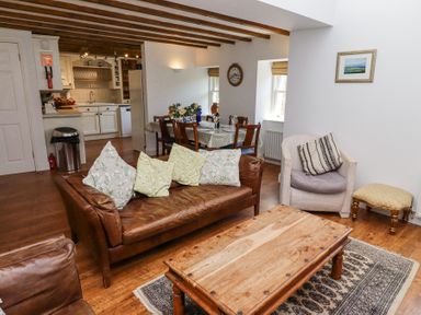 A living room with a wooden coffee table a brown leather sofa and a armchair next to a dining table and kitchen at The Coach House in Lowick near Holy Island