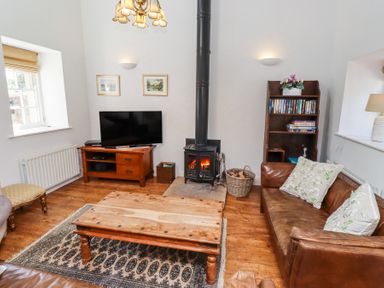 A living room with a wood stove television wooden coffee table bookshelves and leather sofa at The Coach House in Lowick near Holy Island