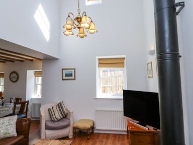 A living room with a chair a television and a chandelier at The Coach House in Lowick near Holy Island