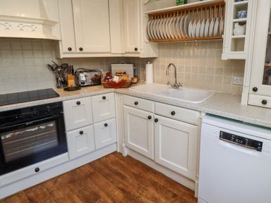 A kitchen corner with oven stove kitchen sink dishwasher countertop with toaster knives and dish rack at The Coach House in Lowick near Holy Island