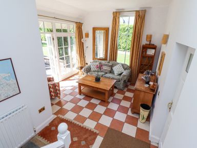 A sitting room with a patterned sofa wooden coffee table and cabinet near large windows at The Coach House in Lowick near Holy Island