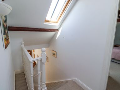 A carpeted staircase with a white banister and skylight window above a hallway with framed pictures at The Coach House in Lowick near Holy Island