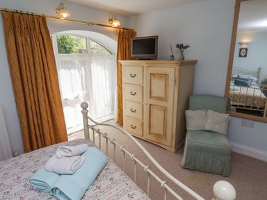 A bedroom with a bed with folded towels a wooden cabinet with a small TV a green chair and a large mirror at The Coach House in Lowick near Holy Island