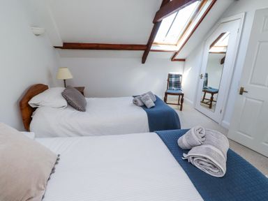 A bedroom with two single beds blue bed runners and folded towels on the beds a chair a bedside table with a lamp and a skylight at The Coach House in Lowick near Holy Island