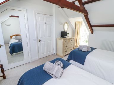 A bedroom with two single beds with blue bed runners and folded towels a chest of drawers with a small television and mirror at The Coach House in Lowick near Holy Island
