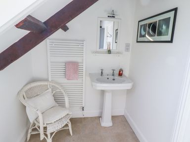A bathroom with a white wicker chair a towel on a radiator a pedestal sink and a framed picture at The Coach House Lowick near Holy Island