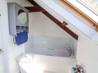 A bathroom with a bathtub under a sloped ceiling and wood beam at The Coach House in Lowick near Holy Island