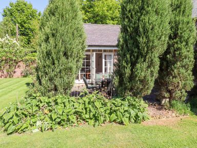 A garden with green bushes and trees and a patio with a table and chairs outside a small building at The Coach House in Lowick near Holy Island
