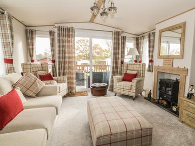 A living room with plaid armchairs sofa matching ottoman and curtains a fireplace and a sliding glass door at 27 Lake View in Cawston