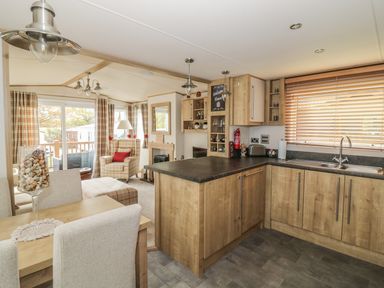 An open plan kitchen and living area with wooden cabinets dining table armchair and large window blinds at 27 Lake View in Cawston