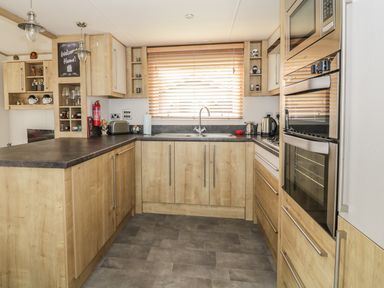 A kitchen with wooden cabinets a black countertop a stainless steel oven microwave toaster and kettle at 27 Lake View in Cawston