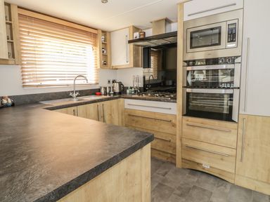 A kitchen with wooden cabinets a window with blinds a double oven a gas stove and a dark countertop at 27 Lake View in Cawston