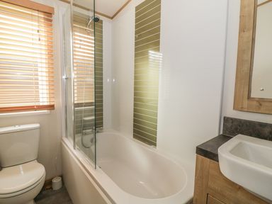 A bathroom with a bathtub shower combination a toilet window with blinds and a sink at 27 Lake View in Cawston