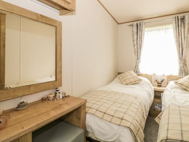 A bedroom with two single beds both with plaid blankets and pillows and a wooden dressing table with a mirror at 27 Lake View in Cawston