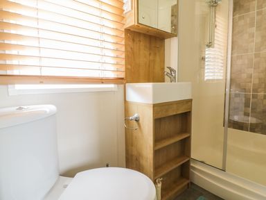 A bathroom with a toilet sink with wooden cabinet and a glass shower enclosure at 27 Lake View in Cawston