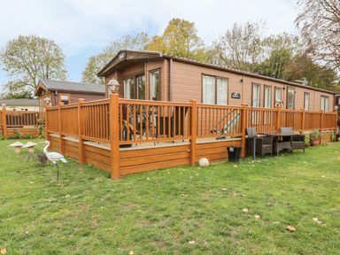 A wooden mobile home with a fenced deck and outdoor chairs on grass at 27 Lake View in Cawston
