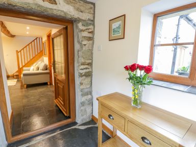 A hallway with a wooden console table and a vase with red roses near a window and a view into a room with a staircase and a sofa at Yr Hen Stabal in Trawsfynydd