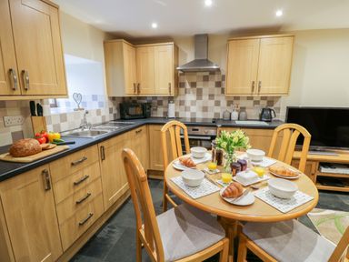 A kitchen with wooden cabinets a dining table set with croissants and orange juice at Yr Hen Stabal in Trawsfynydd