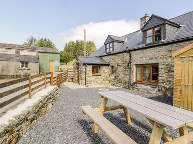 A stone cottage with wooden framed windows and a picnic table on a gravel yard at Yr Hen Stabal in Trawsfynydd