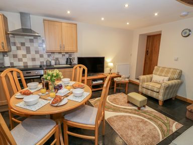 A kitchen and living area with a round dining table set with croissants orange juice and flowers at Yr Hen Stabal in Trawsfynydd