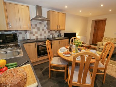 A kitchen with wooden cabinets a dining table set with croissants and a loaf of bread on the counter at Yr Hen Stabal in Trawsfynydd