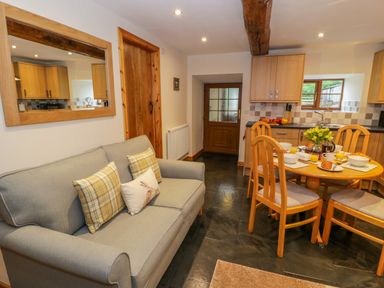 A living area with a gray sofa with cushions and a wooden dining table set with breakfast at Yr Hen Stabal in Trawsfynydd