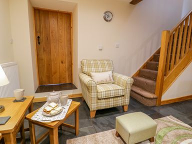 A sitting area with a plaid armchair and a wooden staircase with carpeted steps at Yr Hen Stabal in Trawsfynydd