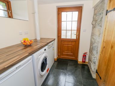 A utility room with washing machine freezer wooden door stone wall and fruit bowl on counter at Yr Hen Stabal in Trawsfynydd