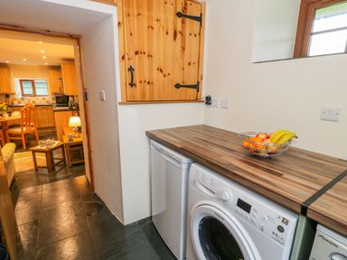 A kitchen area with a washing machine and a small refrigerator under a wooden countertop and a doorway leading to a dining area at Yr Hen Stabal in Trawsfynydd