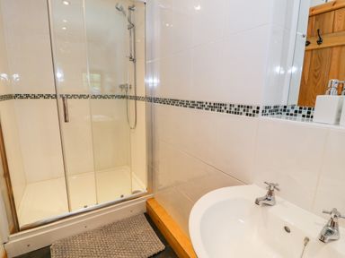 A bathroom with a glass shower enclosure and a white sink with two taps at Yr Hen Stabal in Trawsfynydd