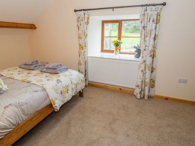 A bedroom with a bed folded towels on it a window with floral curtains and flowers on the windowsill at Yr Hen Stabal in Trawsfynydd