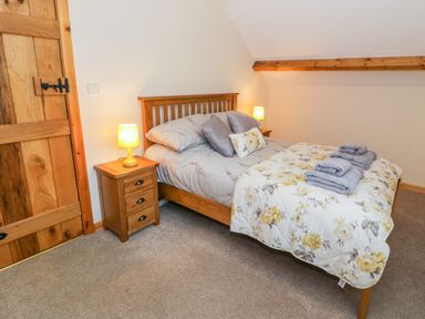 A bedroom with a wooden bed double bedside tables lamps and folded towels on the bed at Yr Hen Stabal in Trawsfynydd