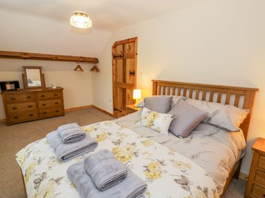 A bedroom with a wooden bed and dresser with folded towels on the bed at Yr Hen Stabal in Trawsfynydd