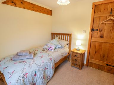 A bedroom with a single bed with floral bedding a bedside table with a lamp wooden door with a hanger on the handle at Yr Hen Stabal in Trawsfynydd