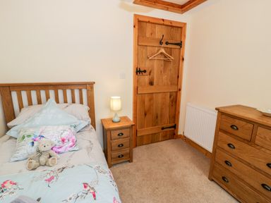A bedroom with a wooden bed a bedside table with lamp a wooden door and a wooden chest of drawers at Yr Hen Stabal in Trawsfynydd