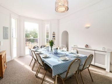 A dining room with a rectangular table covered with a blue polka dot tablecloth set for eight people at Babbacombe Hall in Babbacombe