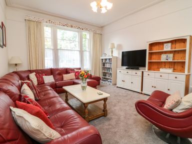 A living room with red leather sofas a coffee table a white cabinet with a television and a lamp at Babbacombe Hall in Babbacombe