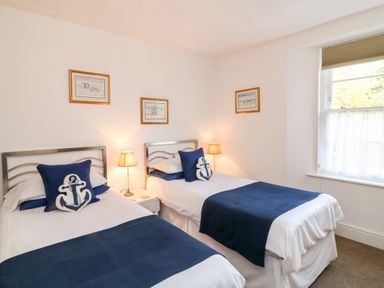 A bedroom with two single beds with blue and white bedding two bedside lamps and framed pictures on the walls at Babbacombe Hall in Babbacombe