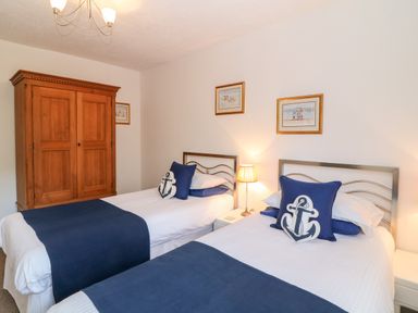 A bedroom with two single beds with blue and white bedding a wooden wardrobe and wall art at Babbacombe Hall in Babbacombe