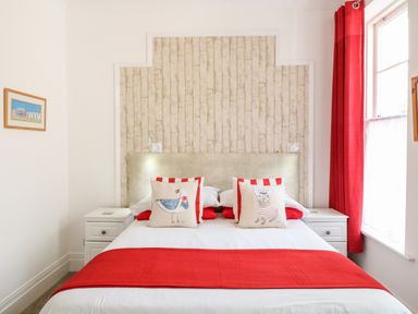 A bedroom with a double bed two bedside tables and red curtains at Babbacombe Hall in Babbacombe