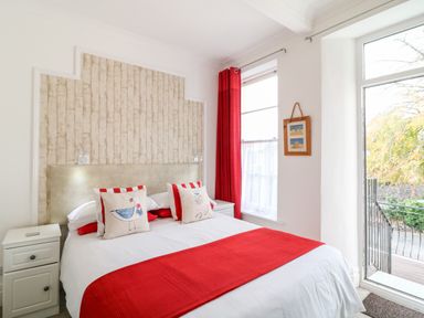 A bedroom with a double bed red accents bedside tables a window with red curtains and a glass door leading outside at Babbacombe Hall in Babbacombe