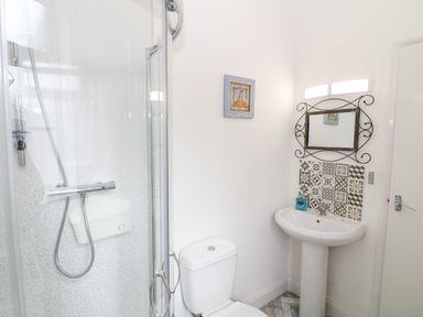 A bathroom with a shower, toilet, pedestal sink, mirror with decorative frame, and patterned tiles behind the sink at Babbacombe Hall in Babbacombe