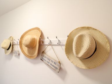 A wall with hooks holding three straw hats and a hanging wooden sign at Babbacombe Hall in Babbacombe