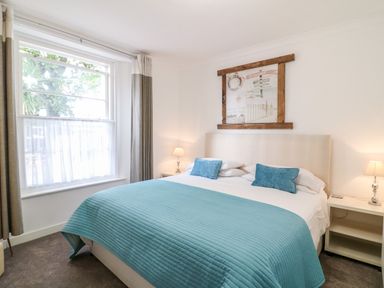 A bedroom with a large bed blue bedding two bedside tables with lamps and a window at Babbacombe Hall in Babbacombe