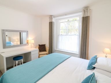A bedroom with a bed with blue pillows and blanket a white desk with a mirror a chair and two lamps at Babbacombe Hall in Babbacombe