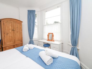A bedroom with a bed rolled towels blue runner wooden wardrobe white desk with mirror blue curtains at Babbacombe Hall in Babbacombe