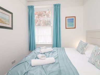 A bedroom with a bed covered in a blue quilt and white towels by a window with blue curtains at Babbacombe Hall in Babbacombe